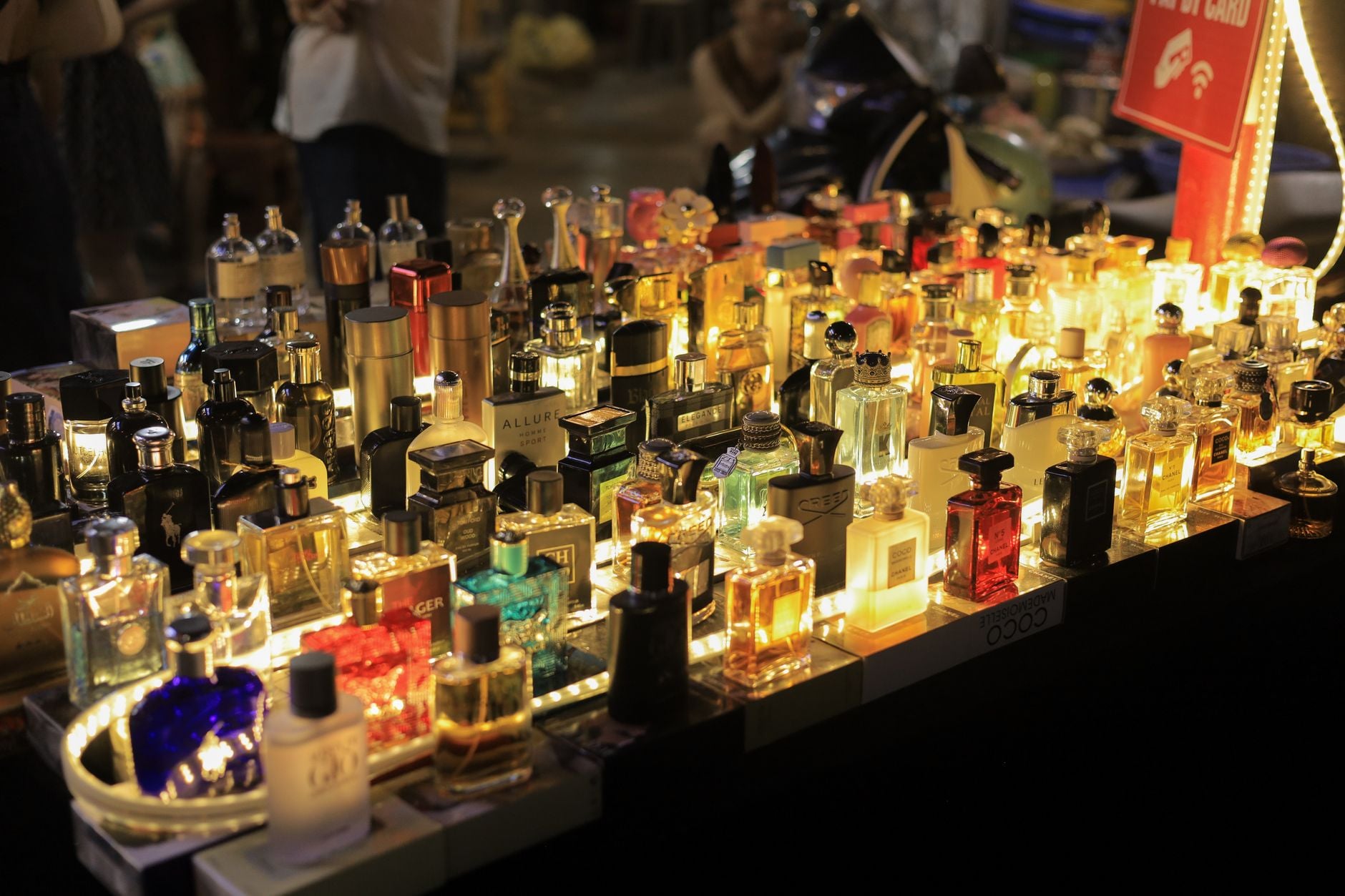 Kolekcja perfum na podświetlanym stole z butelkami w złotych i czarnych opakowaniach