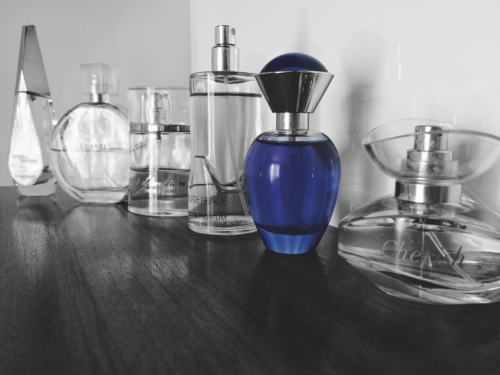Kolekcja różnych flakonów perfum na ciemnej powierzchni, w tym niebieski flakon w centrum z innymi przezroczystymi butelkami perfum dookoła